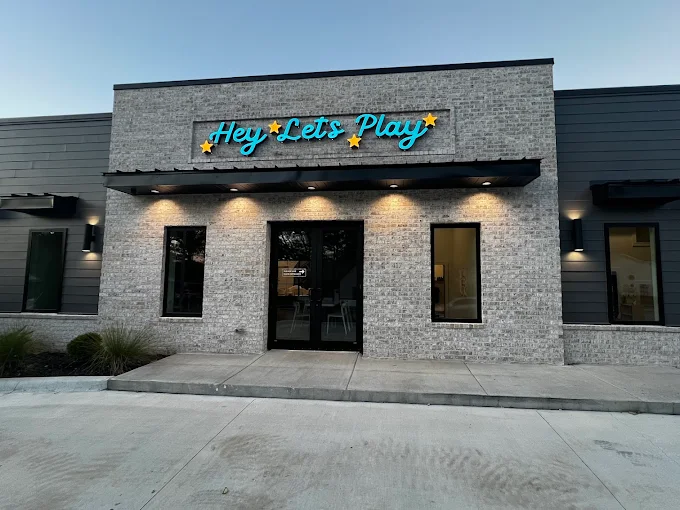 The Hey, Let's Play storefront in Benton, AR with its neon sign lit at dusk